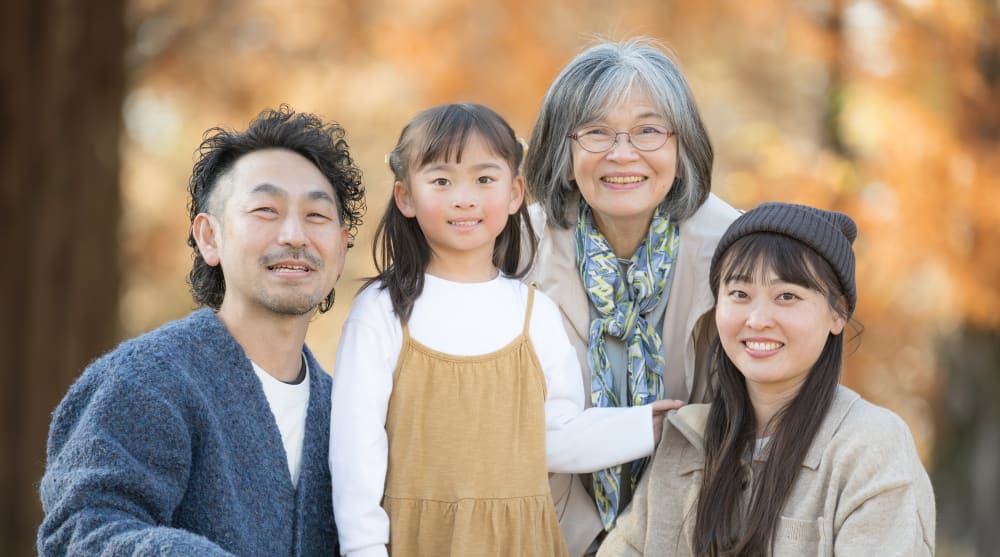 A family of four sits outside in the autumn smiling for the camera.